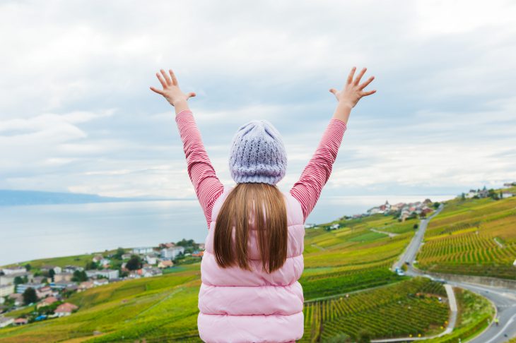 Kid girl stand between Lavaux vineyards looking at the view with arms open