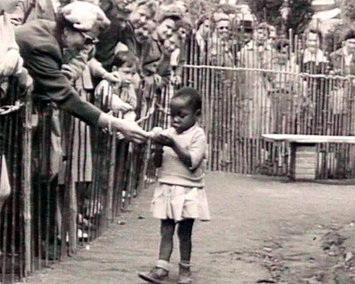 Посетитель в человеческом зоопарке угощает африканскую девочку бананом